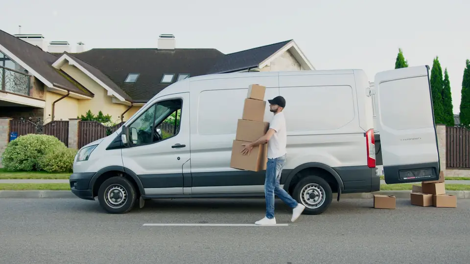 Man carrying a stack of boxes to a white van outside a house